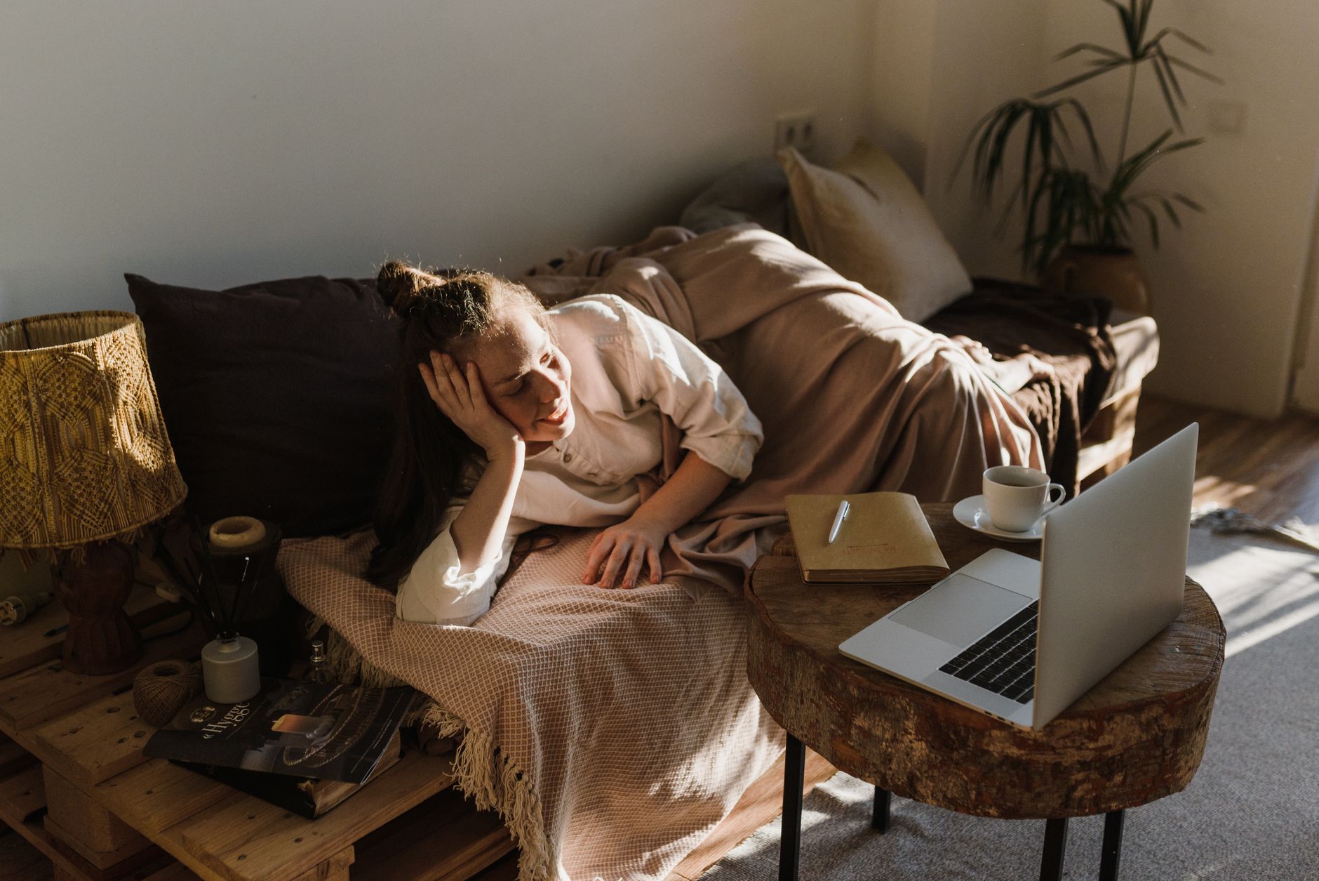 A person resting on a sofa while a laptop remains open on a nearby table