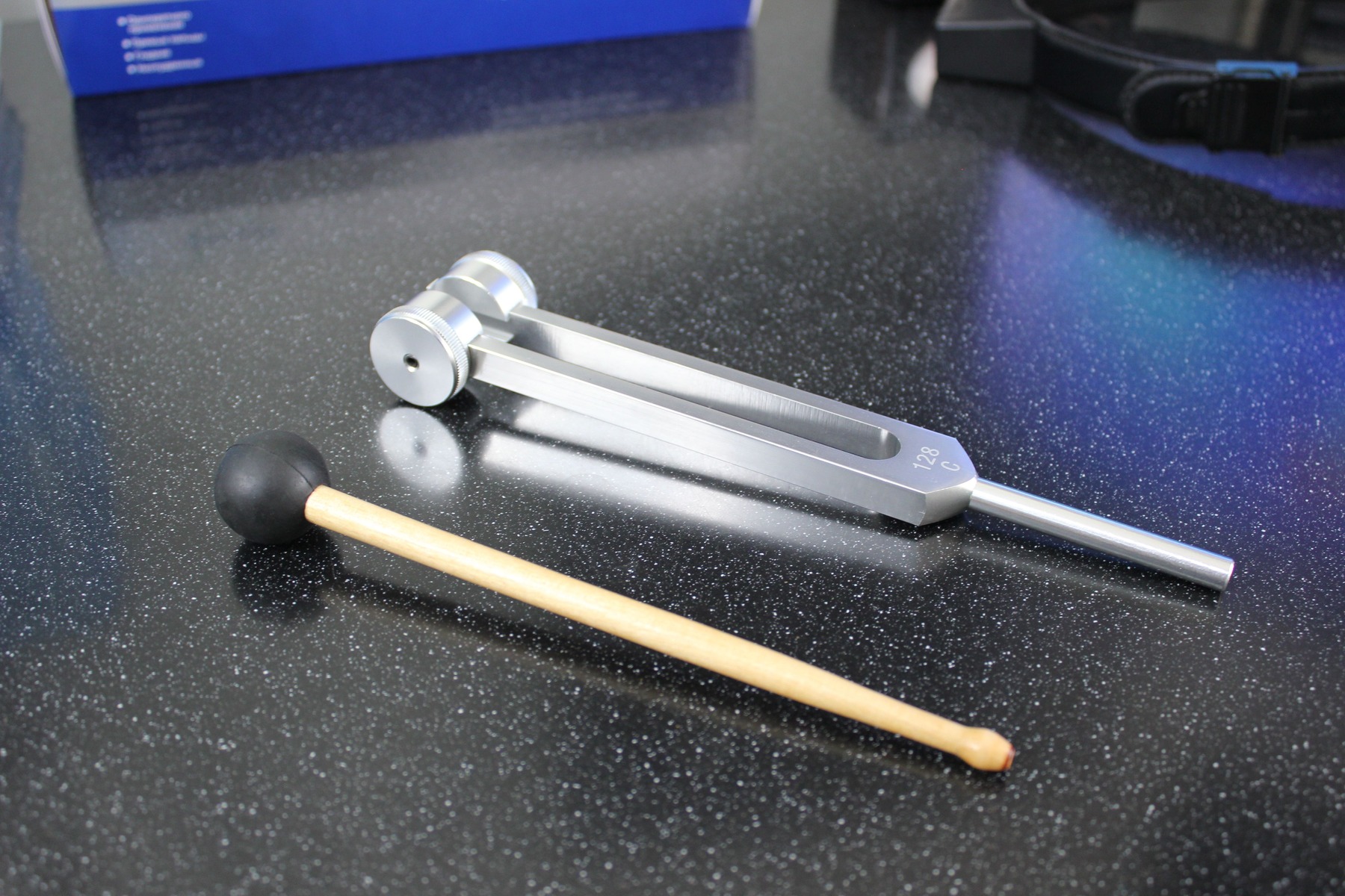 Metal tuning fork and rubber-tipped mallet on a dark laboratory table