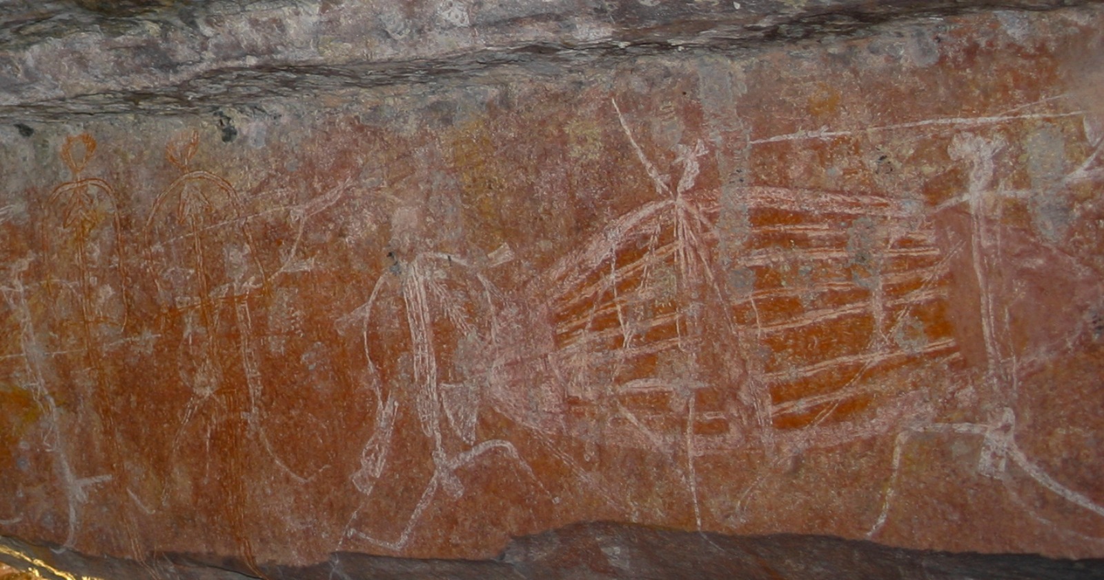 White and ochre X-ray style rock paintings of human figures and a large fish on red sandstone at Ubirr in Kakadu National Park
