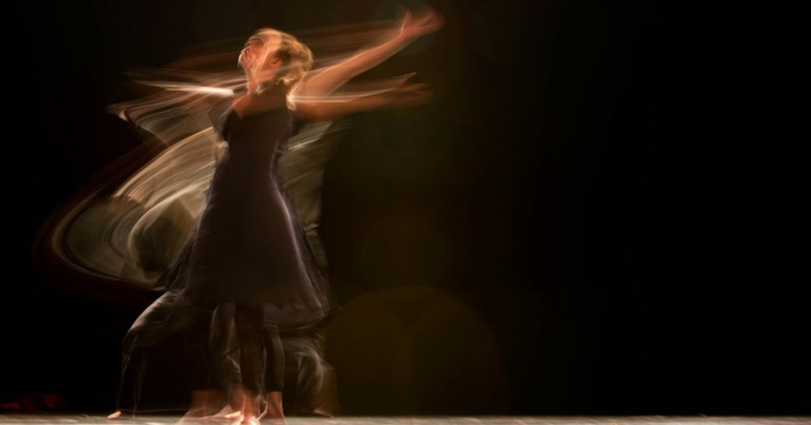 A dancer in a dark dress spins on a stage, her arms blurred by motion