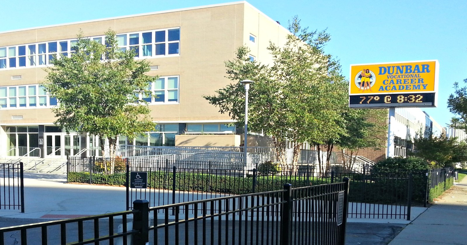 The three-storey Dunbar Vocational Career Academy building behind a black iron fence, with its sign showing the time and temperature.