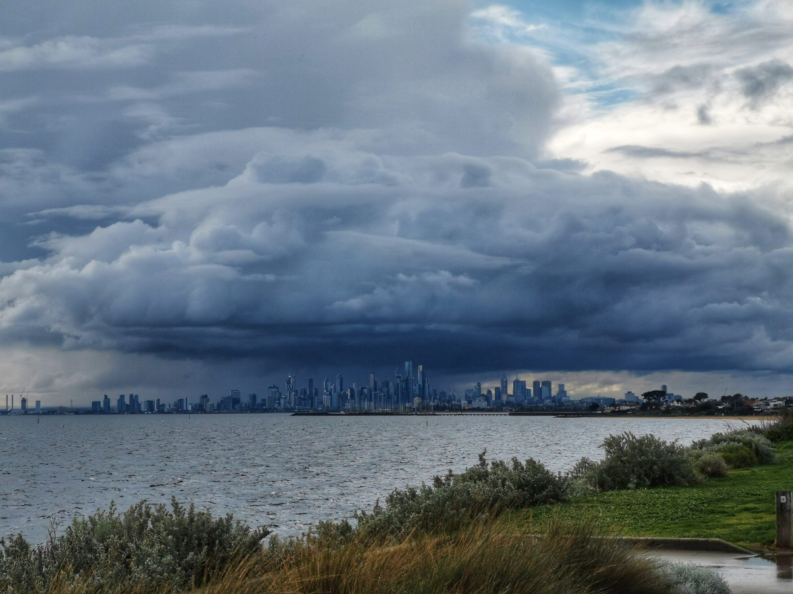 Dark storm clouds gathering above the Melbourne city skyline, with patches of blue sky