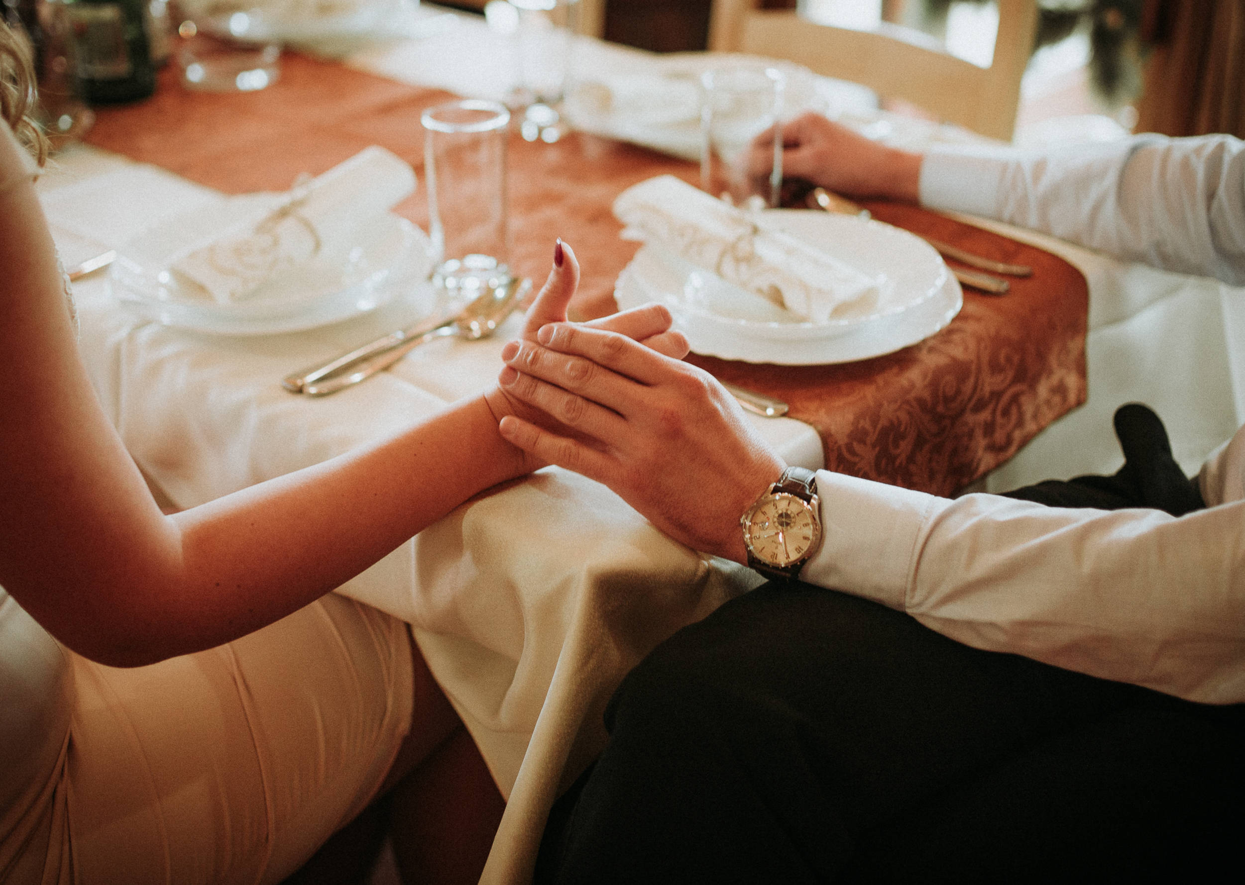Two people holding hands across a set wedding table